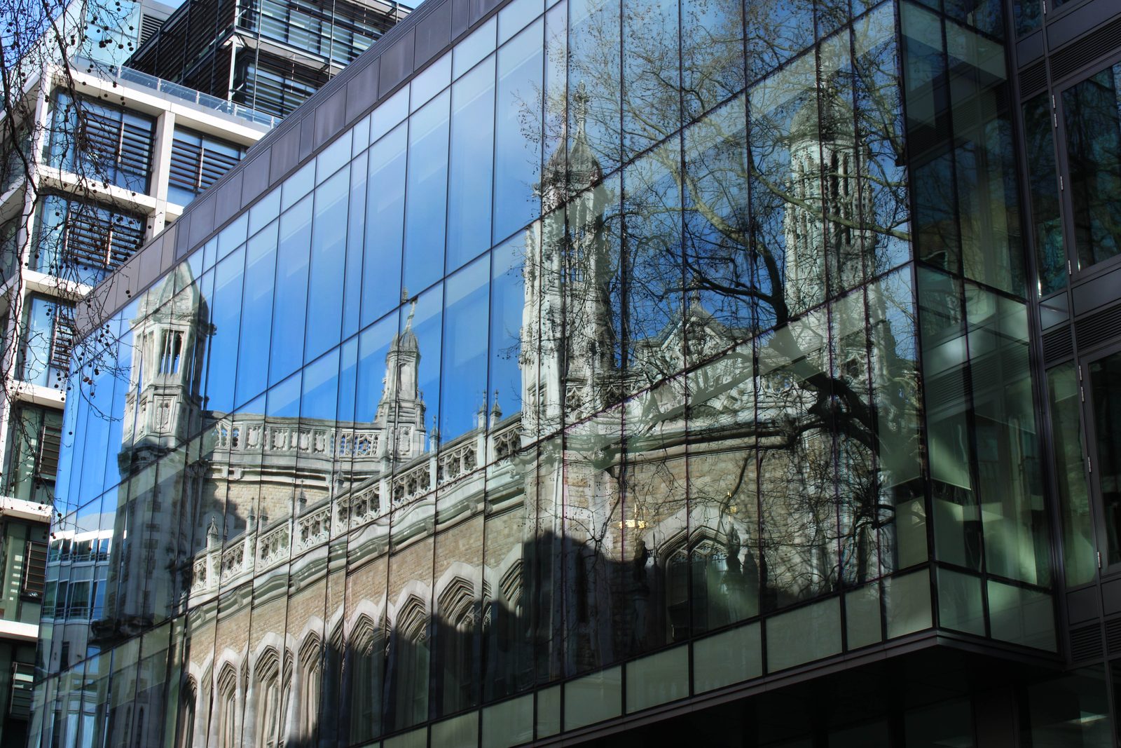 The gothic stonework, towers and pinnacles of a court building reflected across the glazed facade of a modern office opposite.