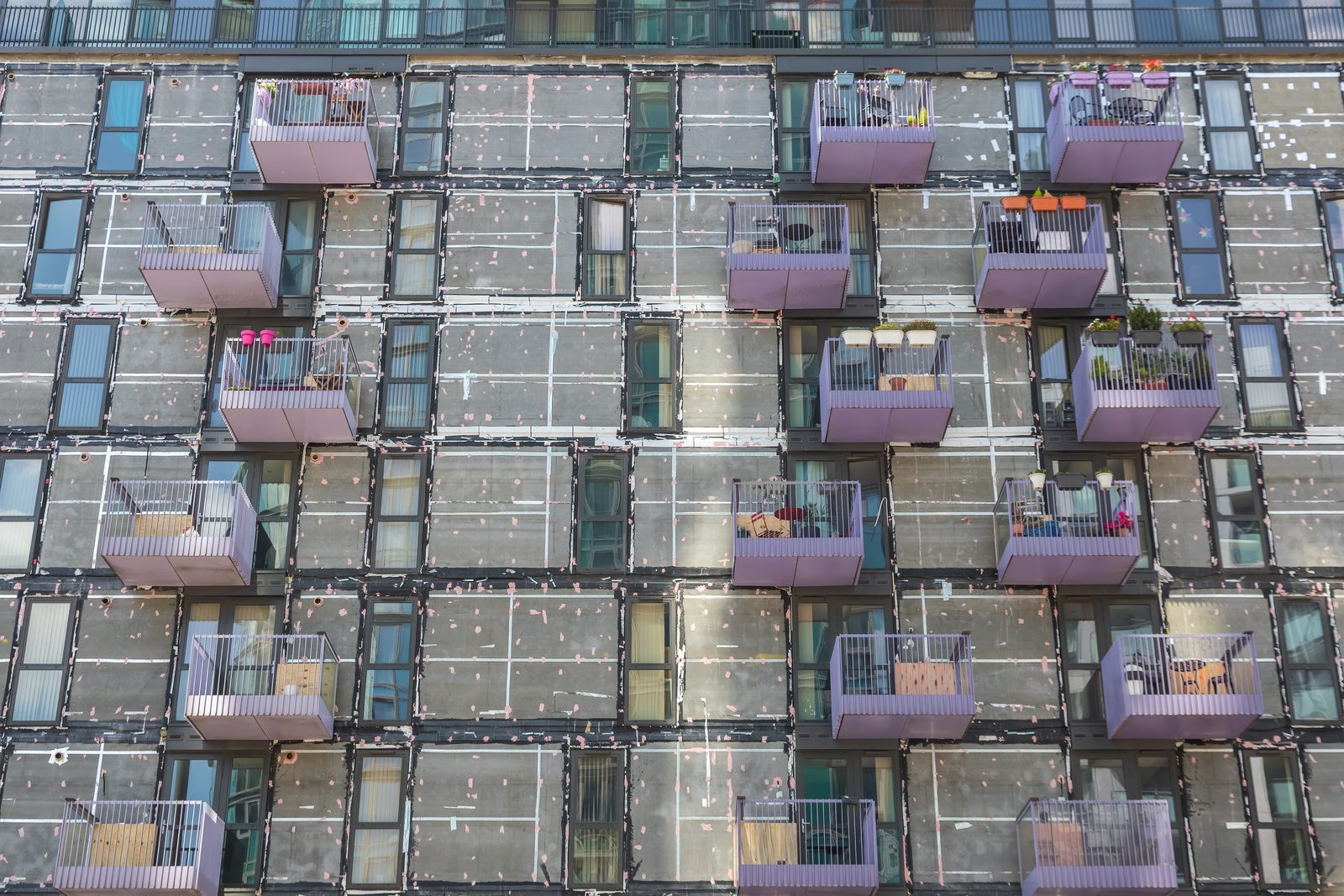 The facade of an occupied residential block with the external wall cladding and insulation stripped back to the sheathing, balconies and windows in use.