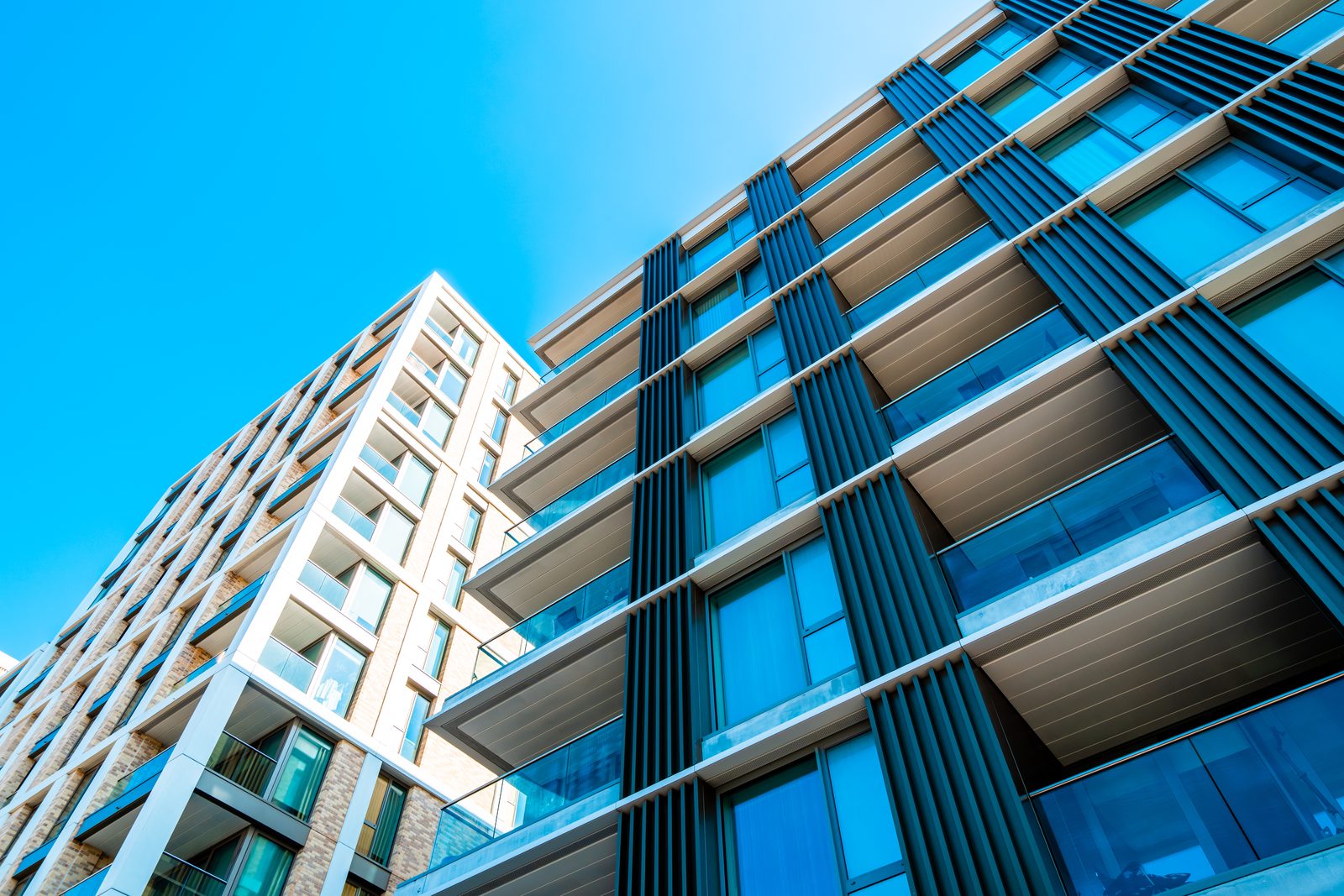 Two modern apartment buildings seen from street level against a clear sky, one in brick and one in glass and metal fins.