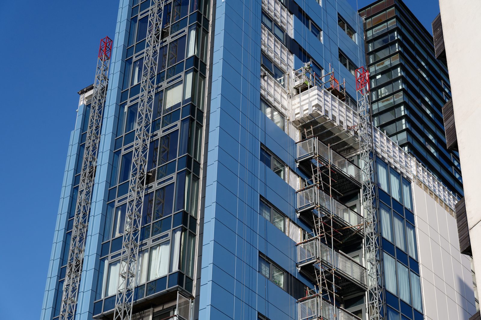 Mast climbing work platforms and an access deck rigged against the glazed facade of a residential tower.